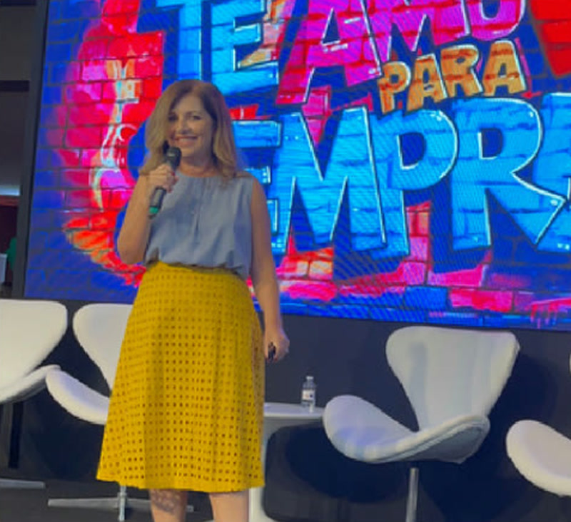 Claudia Fernandes no palco, com o telão da palestra Te Amo Para Sempre ao fundo